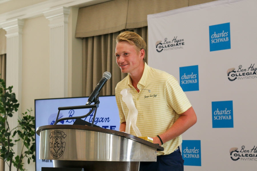 A young man stands at a podium with a glass golf trophy in front of him.