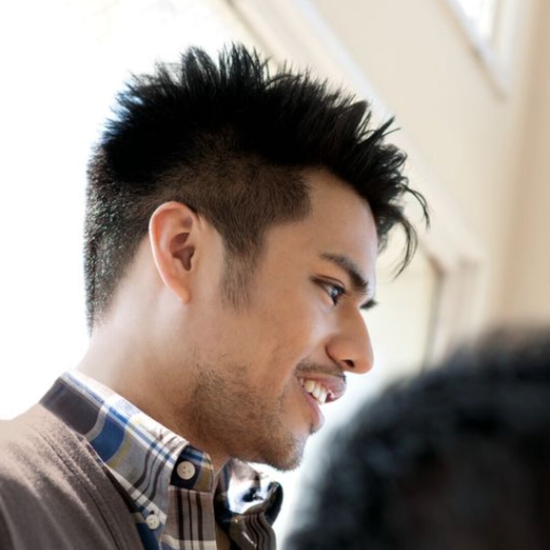 Hispanic man with a modern haircut in button up shirt smiling.