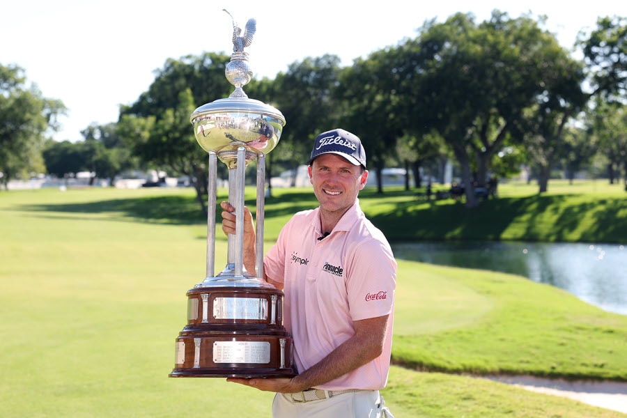 Russell Henley poses with the Charles Schwab Challenge trophy on the golf course.