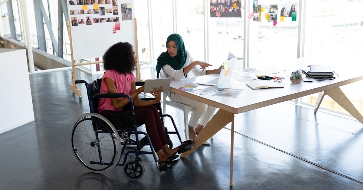 Two women, one in a hijab and one in a wheelchair, having a conversation.