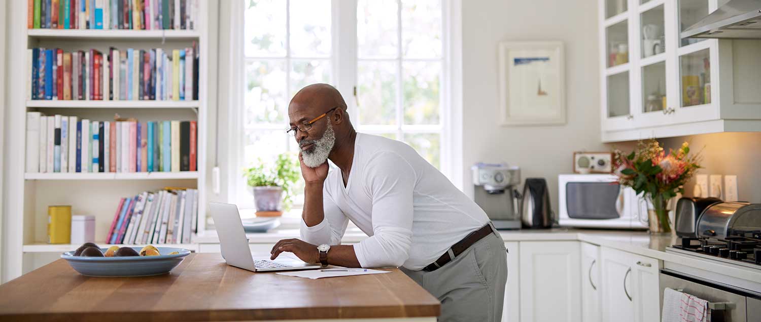 Man looking at his laptop in his kitchen.