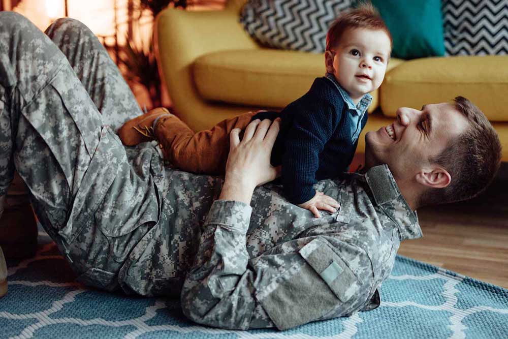 Father in military uniform holding his son on the floor.