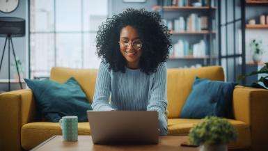 A woman sitting on the couch with a laptop on the coffee table in front of her.