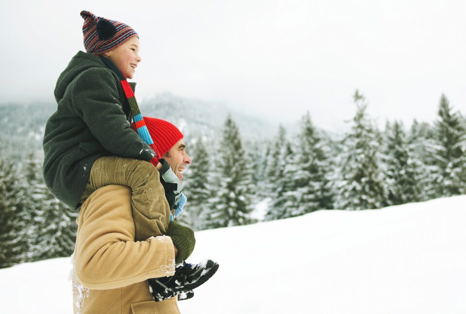 Man with son perched on shoulders in a snowy field.