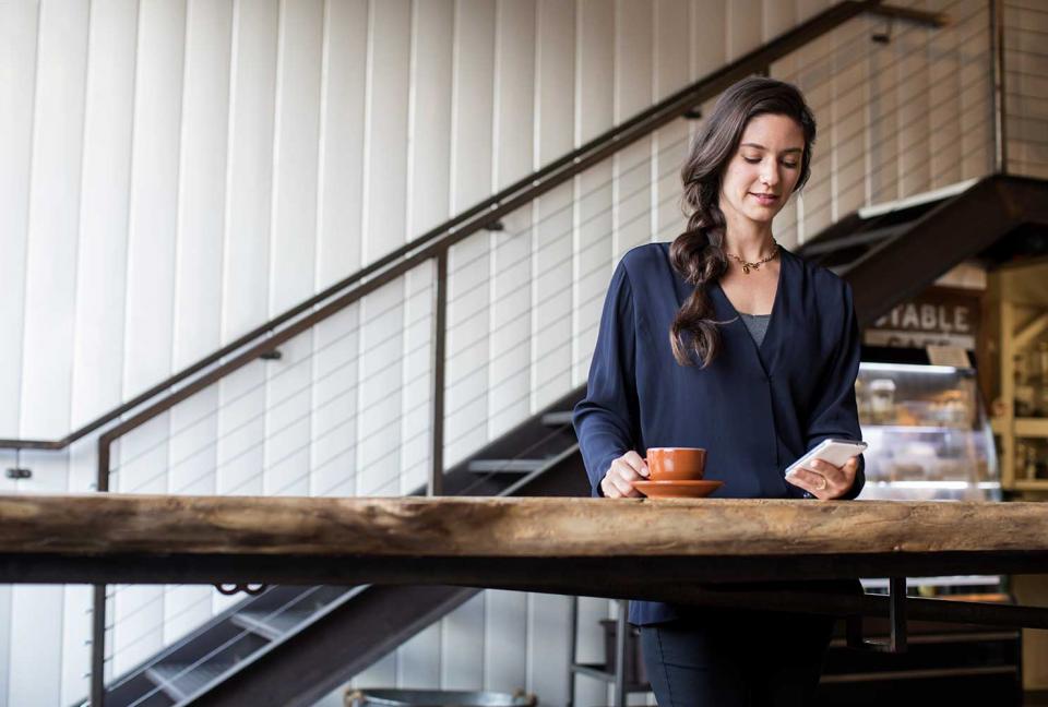 Woman looking at her phone while having a cup of coffee.