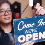 Lady hanging a 'We're Open' sign